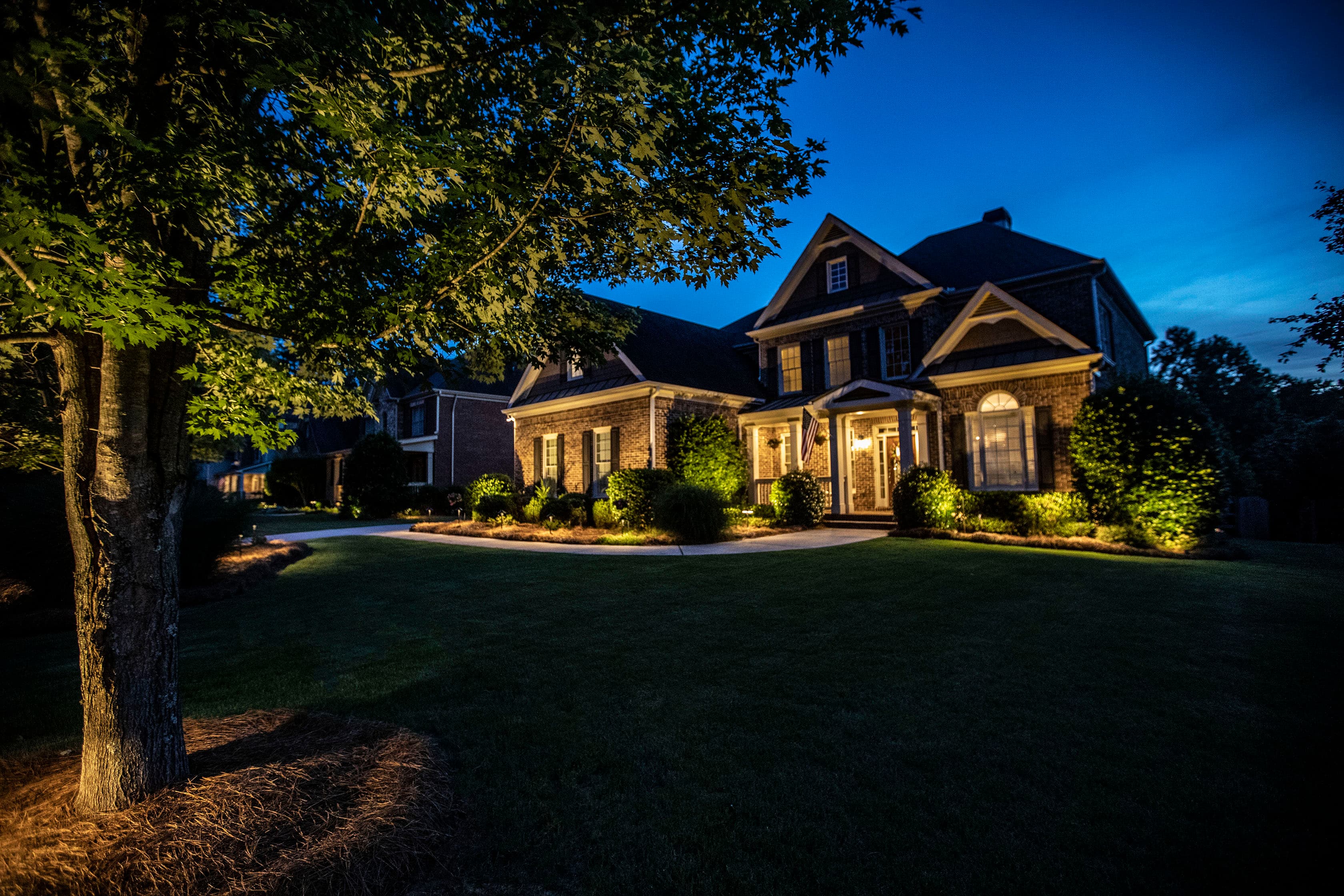 Stunning brick home at twilight with comprehensive landscape lighting including tree uplighting, pathway lights, and architectural lighting in Auburn Alabama
