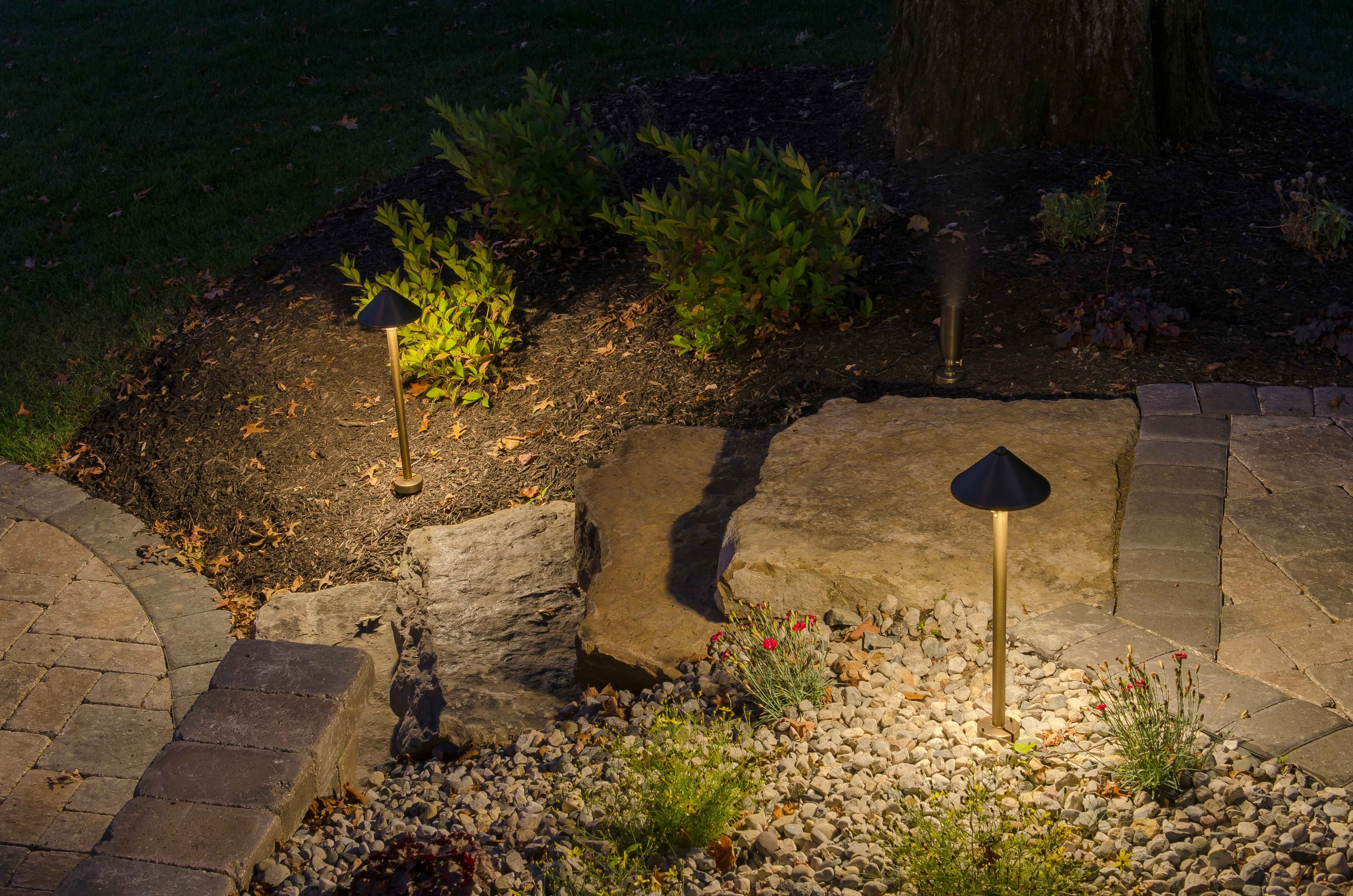 Night shot of brass path lights illuminating landscaping with large boulders, ornamental grasses, and paver pathway in Auburn Alabama
