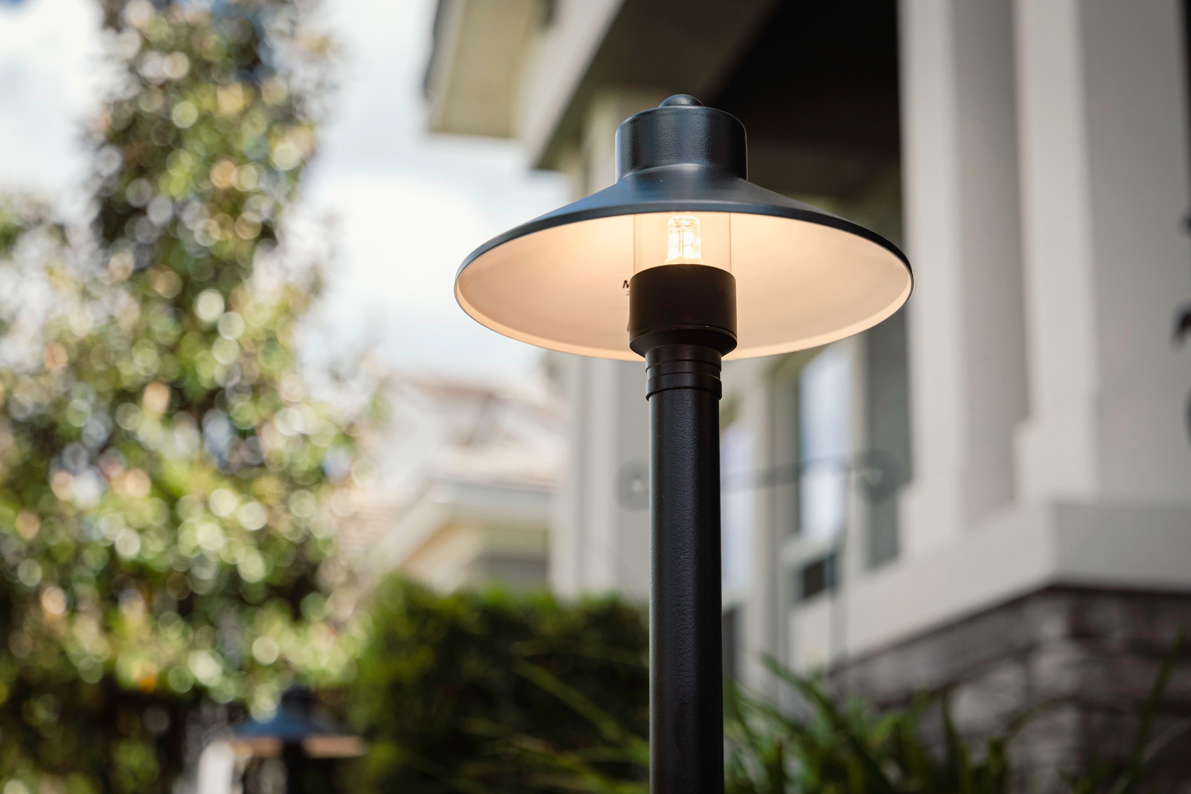 Close-up of modern black path light fixture with wide hat-style shade in daytime showing quality design and craftsmanship