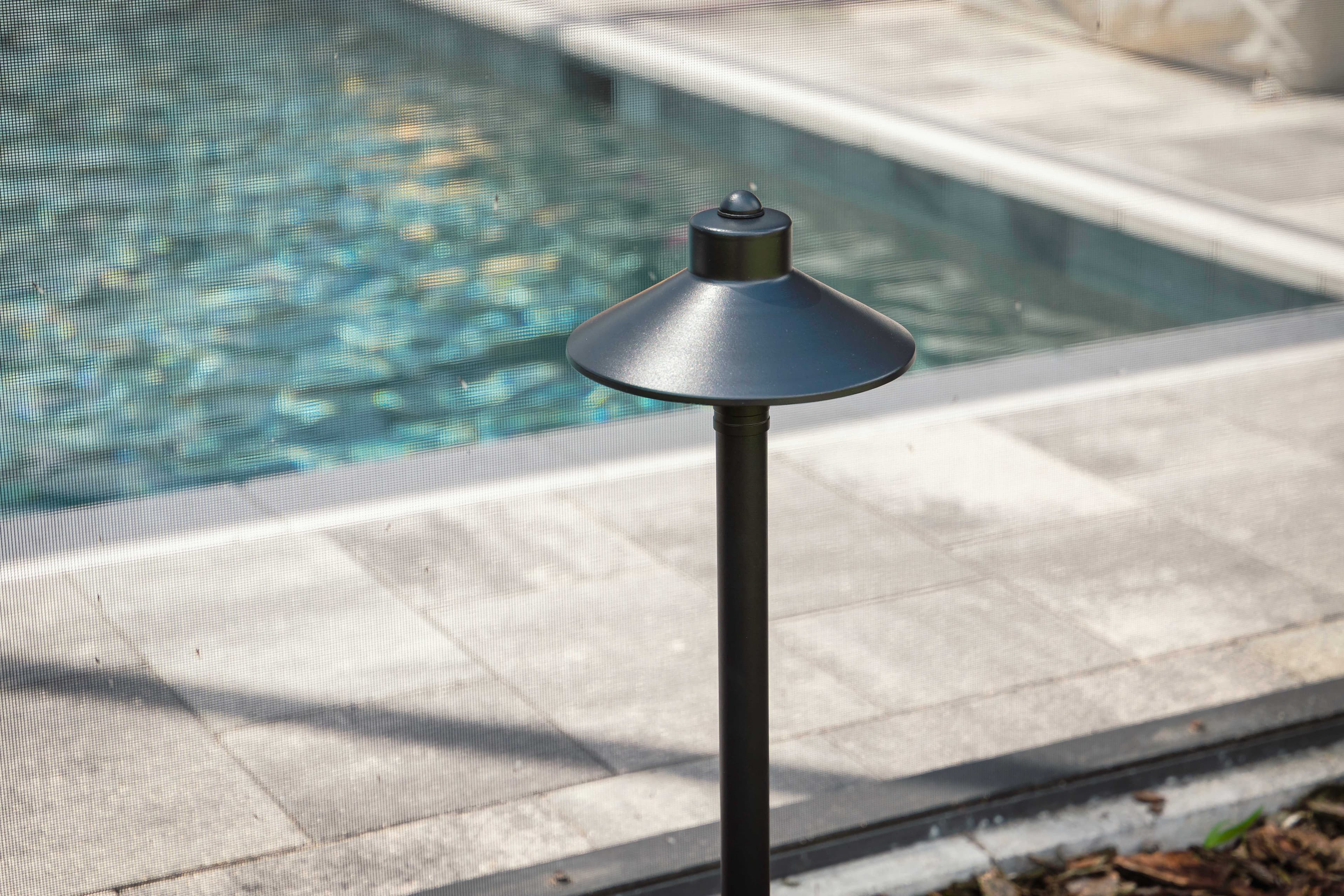 Close-up of modern black path light fixture next to pool with screen enclosure showing quality installation in Auburn Alabama