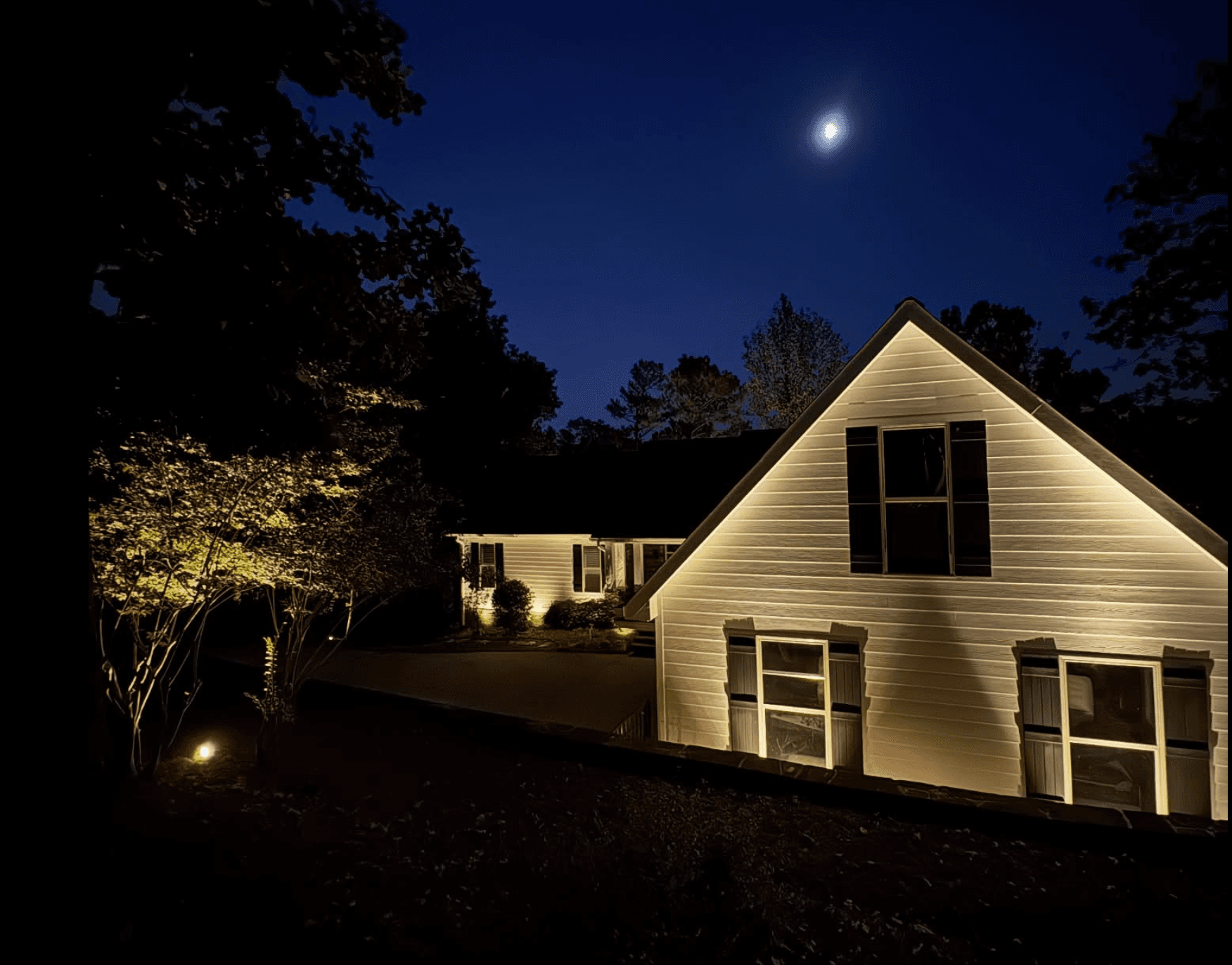 White home with tree uplighting under moonlight