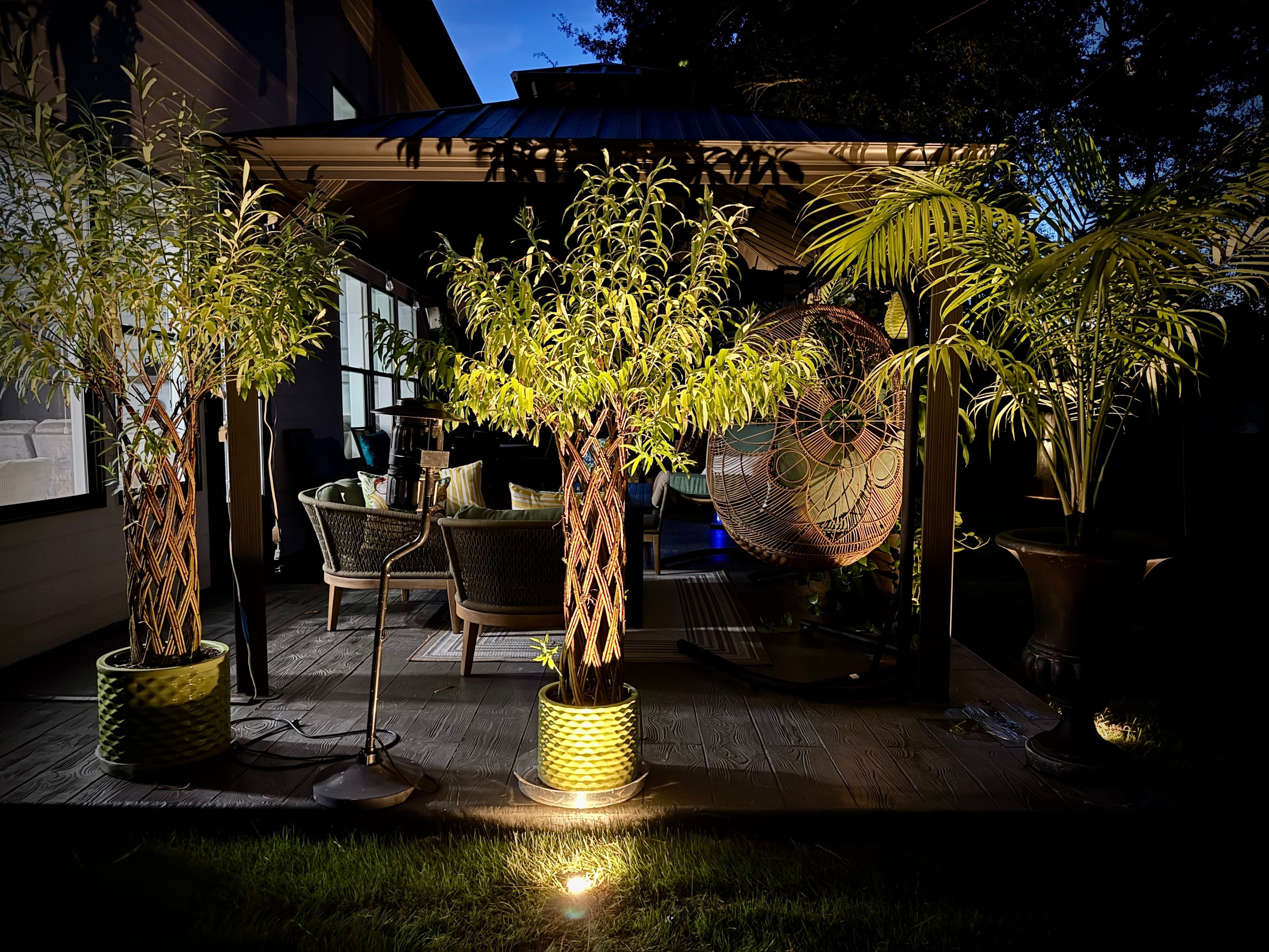 Evening patio with uplighted palm planters, wicker furniture, and ambient outdoor lighting design