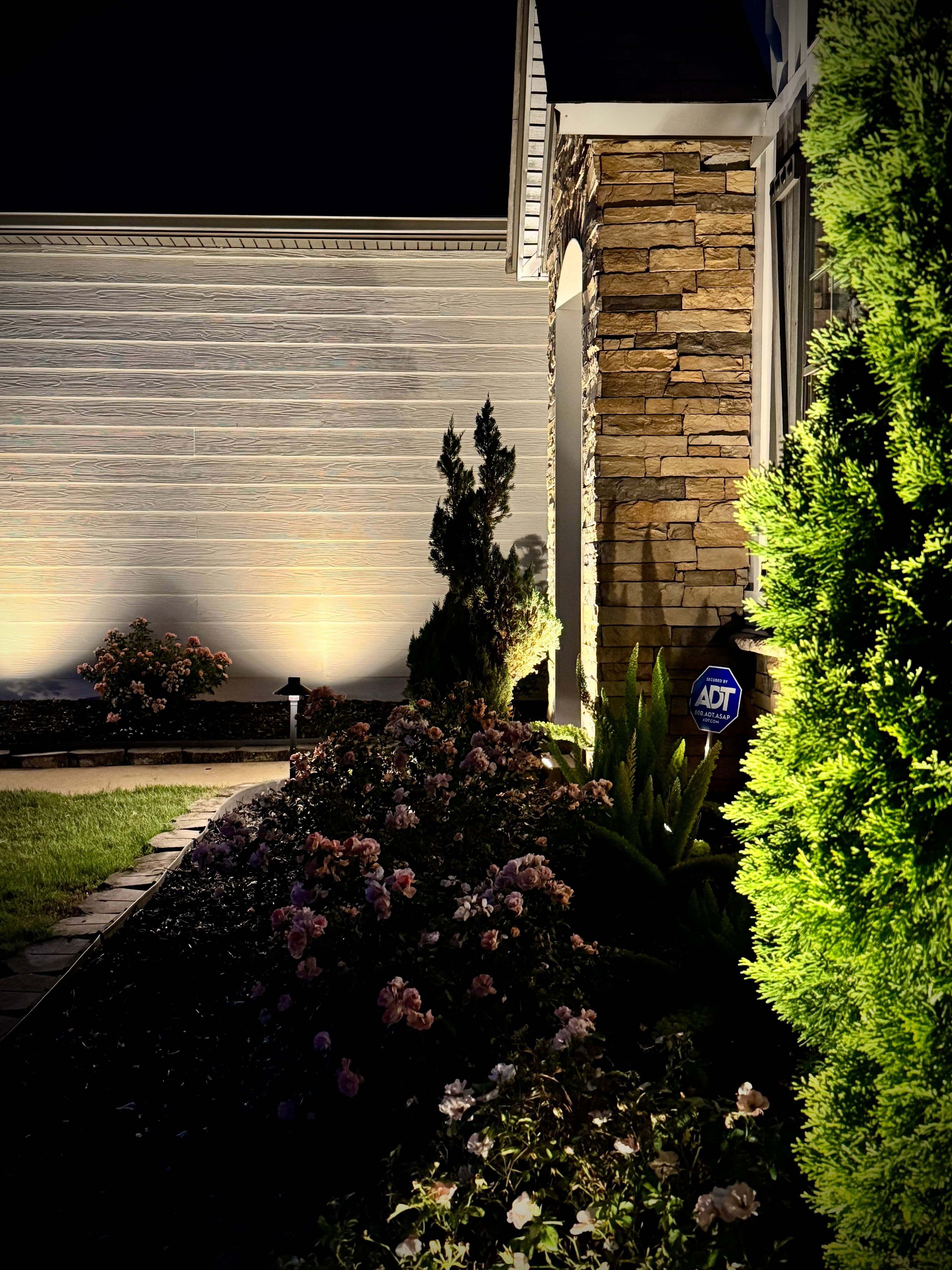 Home garage and entrance at night with uplighted stone columns, landscape lighting, and architectural accent lights
