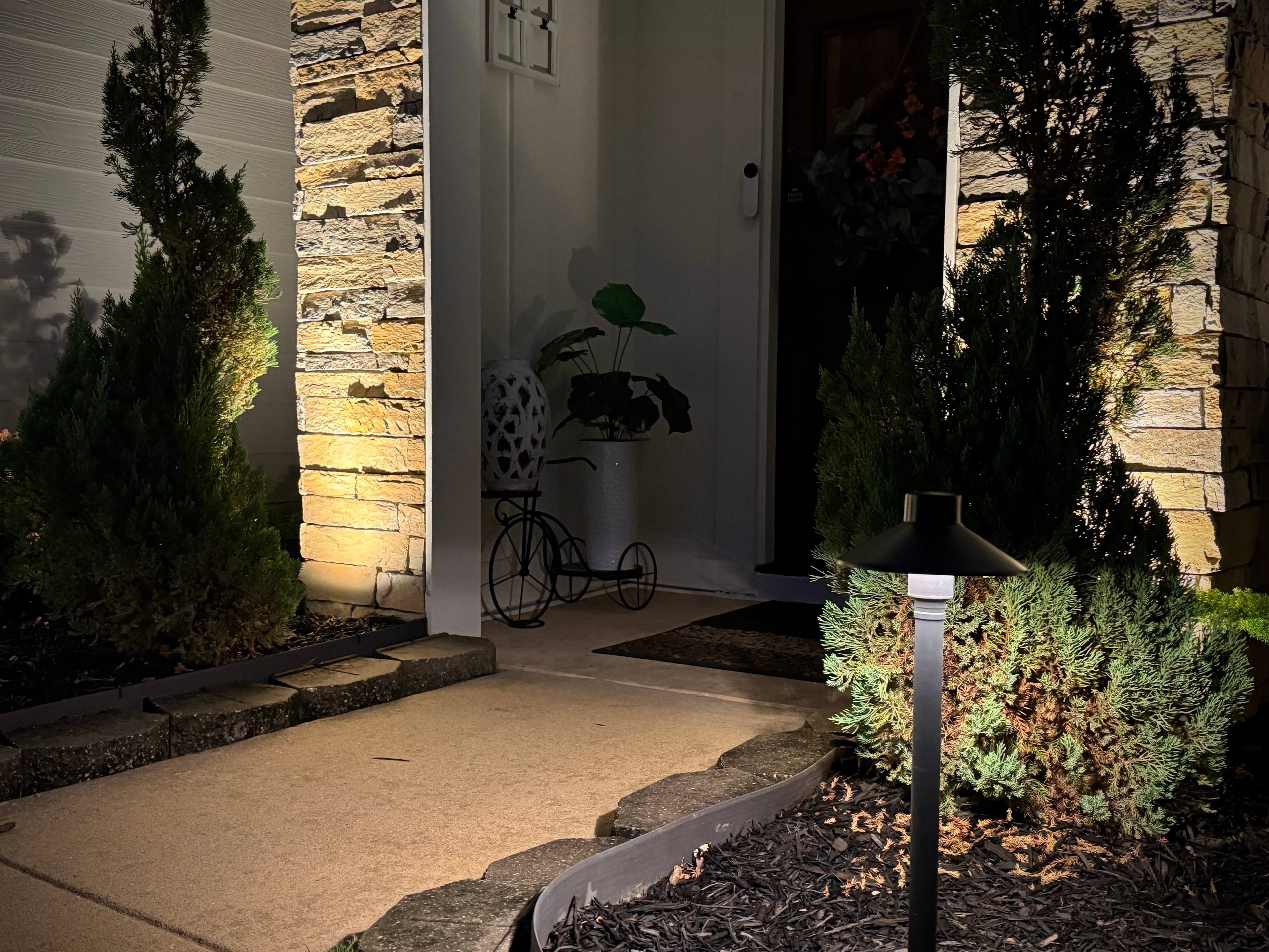 Home entrance at night featuring illuminated stacked stone walls, pathway lighting, and landscape bed lights
