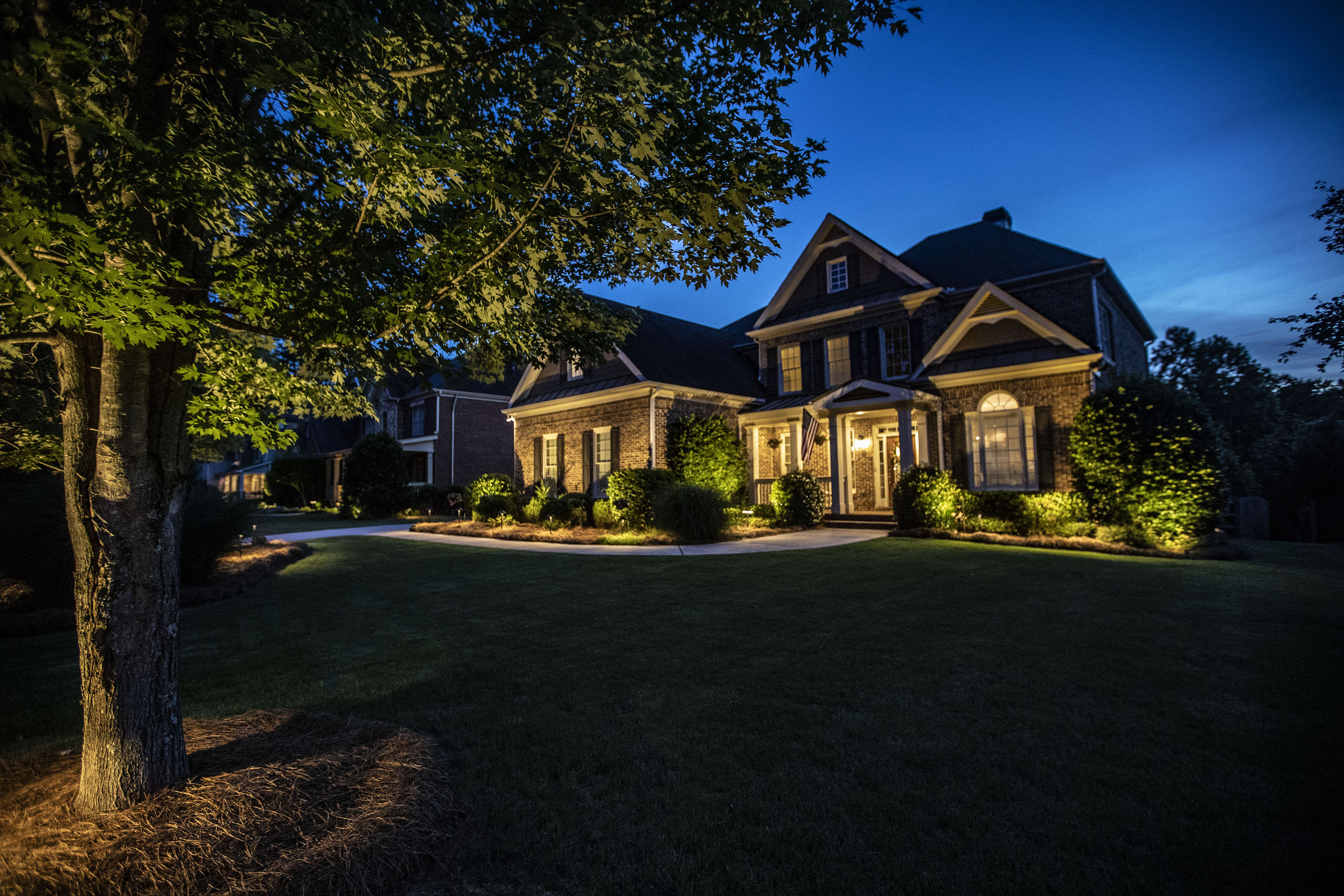 Twilight Comprehensive Lighting Design Stunning brick home at twilight with comprehensive landscape lighting including tree uplighting, pathway lights, and architectural lighting in Auburn Alabama